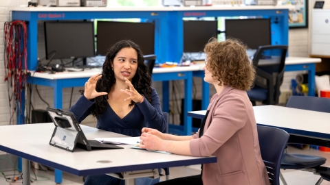 Aura Chuck Hernandez sits at a table conversing with Professor Annie Ross.