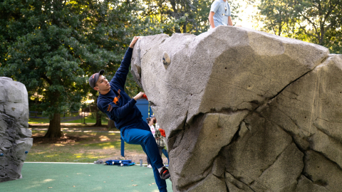 A student in a blue shirt climbs on a boulder in Bucknell's bouldering park.