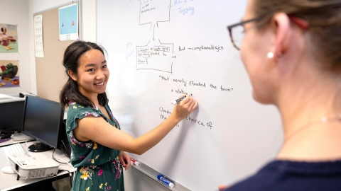 Sanda Tan writes on a whiteboard while Professor Heidi Lorimor stands in the foreground.