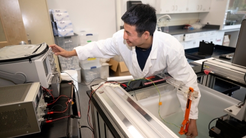 Student Tobey Kim with in a lab wearing a white lab coat and performing a test