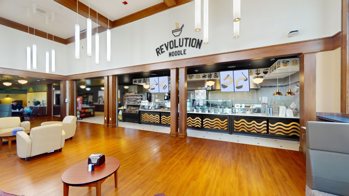 An artist rendering of an Asian takeout restaurant in MacDonald Commons. A sign stating Revolution Noodle appears above a serving counter with instant noodle patterns along the front. A lounge area with leather chairs is in the foreground.
