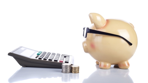 A piggy bank next to a calculator and stack of coins