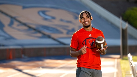 Michael Hardyway '25 wears an orange Bucknell shirt and holds a football as he smiles in Christy Mathewson Memorial Stadium.