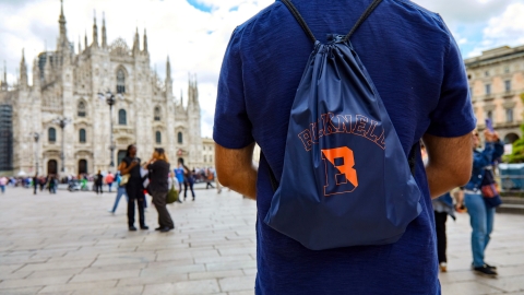 Bucknell student in a square in Milan. Student is facing away from the camera, wearing a Bucknell backpack. Cathedral in background. 