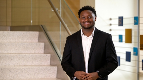 Jerimaha McClain wears a dark suit and white dress shirt and stands at the base of a stairway in Holmes Hall.