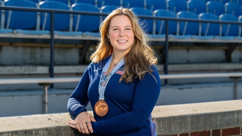 Evelyn Bliss stands on the lower level of a stadium wearing a blue Bucknell shirt and a bronze medal around her neck.