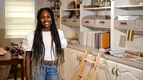 Chrissy Haney Scheimreif ’16 wears a white shirt and jeans and stands in her home office/studio while smiling.
