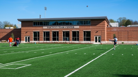 A football kicker practices on the turf in front of the Michael C. Pascucci ’58 Team Center