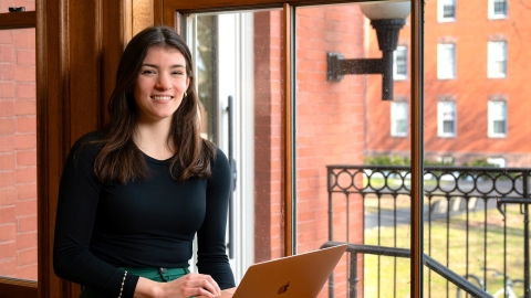 Sarah Downey works on her laptop in front of a large window.