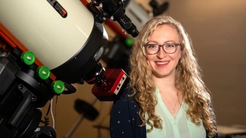 Professor Jackie Villadsen stands next to a large telescope on Bucknell&#039;s campus and smiles.