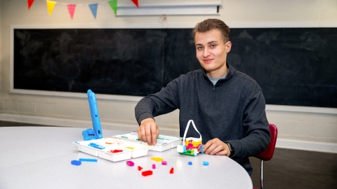 Aiden Cherniske '27 sits at a table and smiles with colorful components of robotics materials in front of him. 