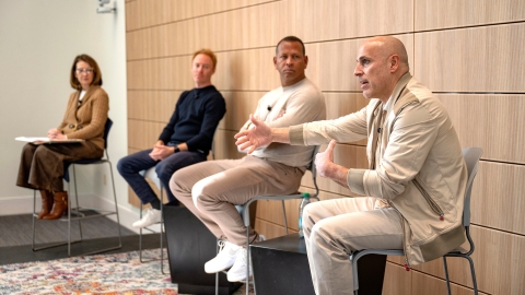 Marc Lore '93 sits on a chair on a stage and gestures with his hand as Alex Rodriguez, Jordy Leiser '06 and Dean Michelle Roehm, also in chairs on the stage, look at Marc.