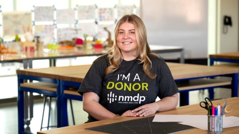 Kate Ellis '25 sits at a desk in a classroom wearing an "I'm a Donor T-shirt."