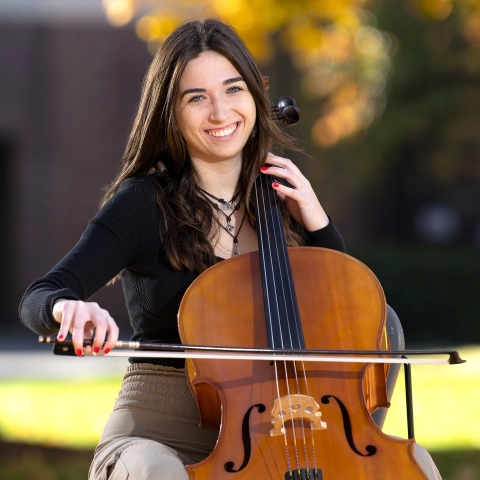 Student Elle Chrampanis sits outside playing the cello