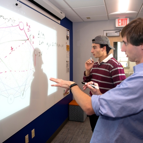 Sam Gutekunst stands at a whiteboard with a student