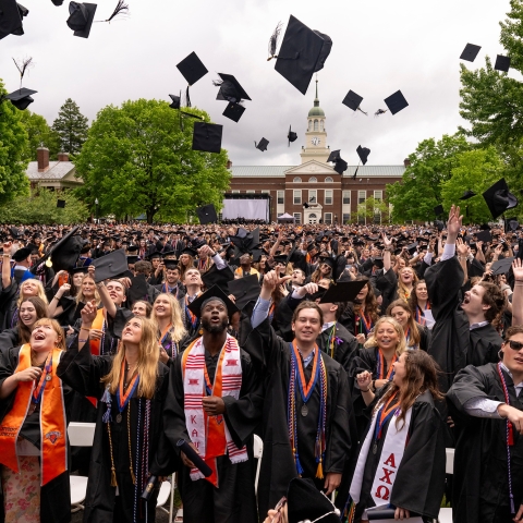 Celebratory members of the Class of 2024 toss their graduation caps in the air and cheer and smile.