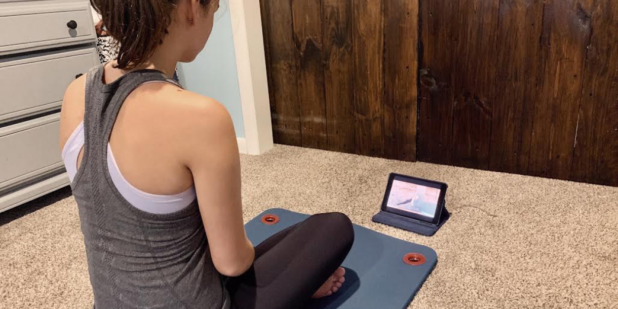 A student sits on a yoga mat in front of a tablet.