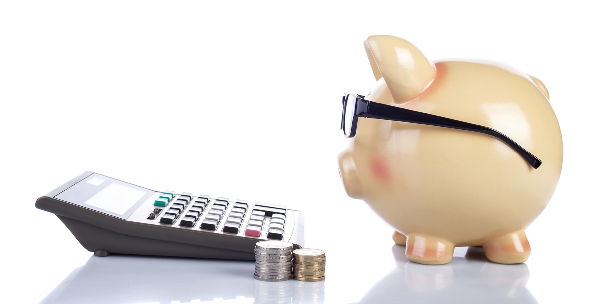 A piggy bank next to a calculator and stack of coins