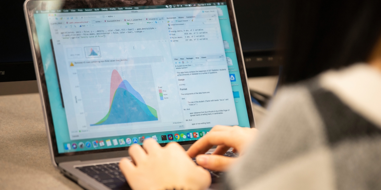 A student's hands are seen in the keyboard of a laptop showing a graph.