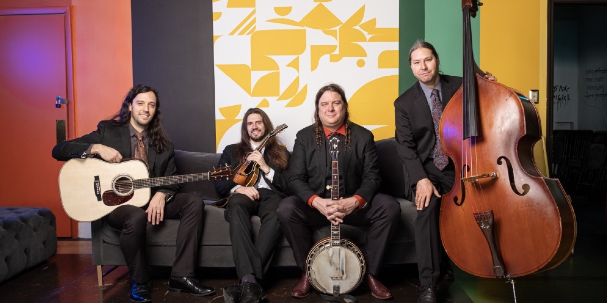 Members of Henhouse Prowlers sit on a couch facing the camera, each holding their instrument