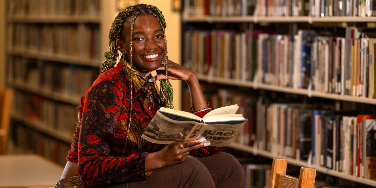 Athaliah Elvis smiles with an open book in her hand and book stacks in the background.