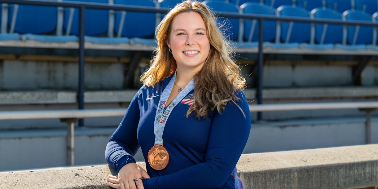 Evelyn Bliss stands on the lower level of a stadium wearing a blue Bucknell shirt and a bronze medal around her neck.