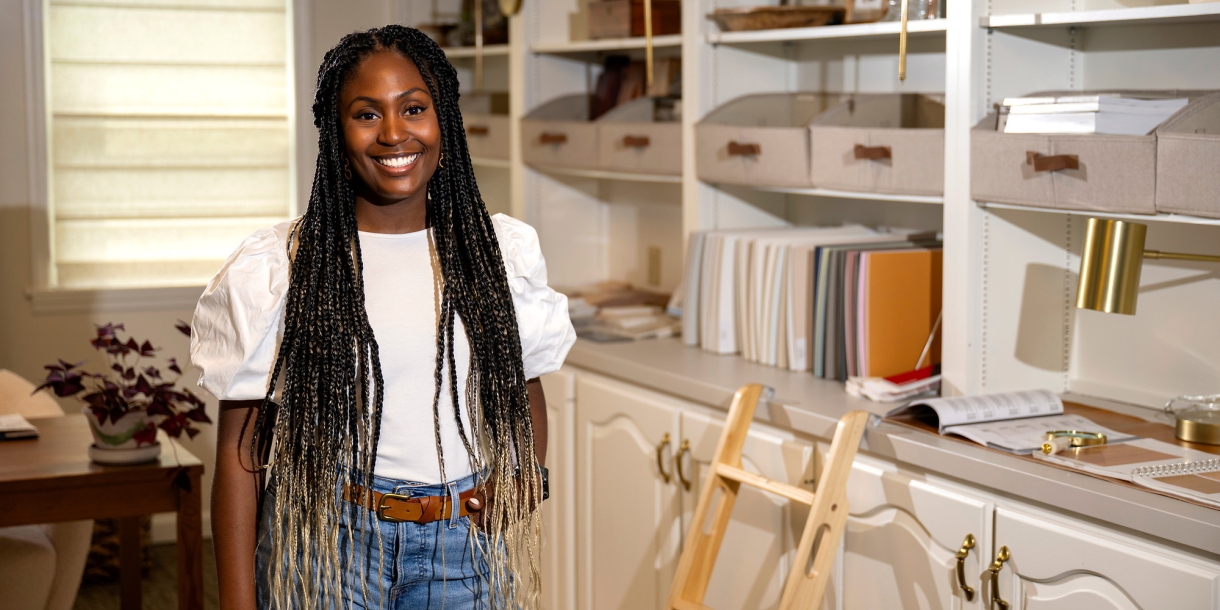 Chrissy Haney Scheimreif ’16 wears a white shirt and jeans and stands in her home office/studio while smiling.