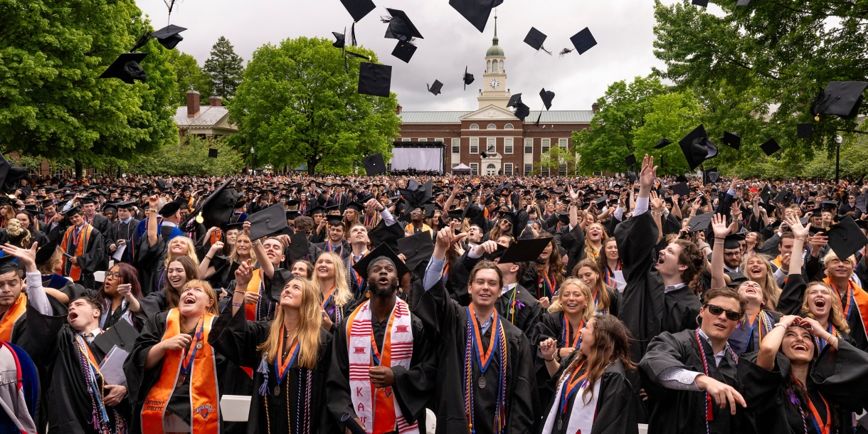 Celebratory members of the Class of 2024 toss their graduation caps in the air and cheer and smile.