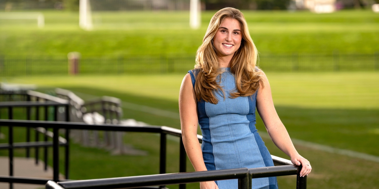 Lea Tarzy &#039;24 poses in a blue dress in the stands of a soccer field.