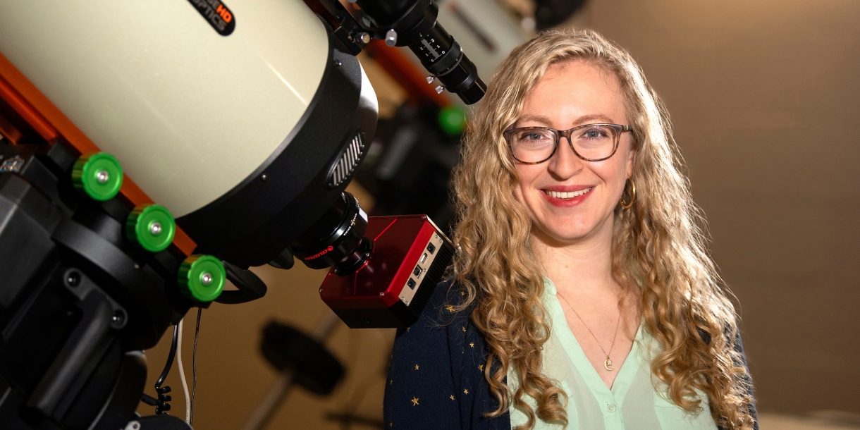 Professor Jackie Villadsen stands next to a large telescope on Bucknell&#039;s campus and smiles.