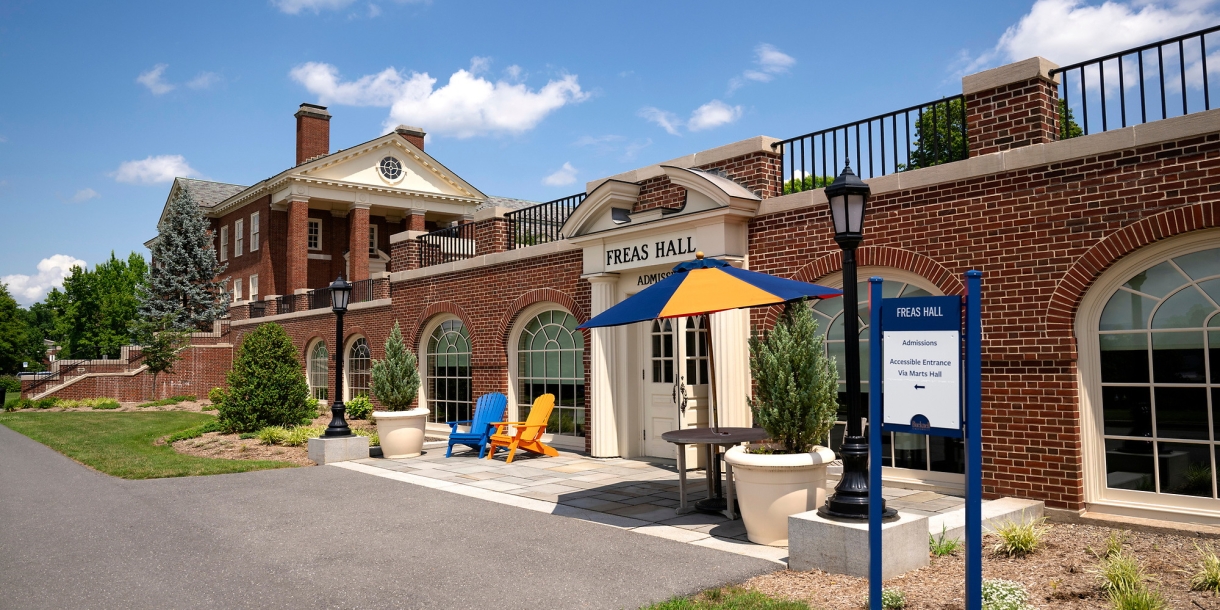 A pair of blue and orange adirondack chairs sit near the entrance of Freas Hall.