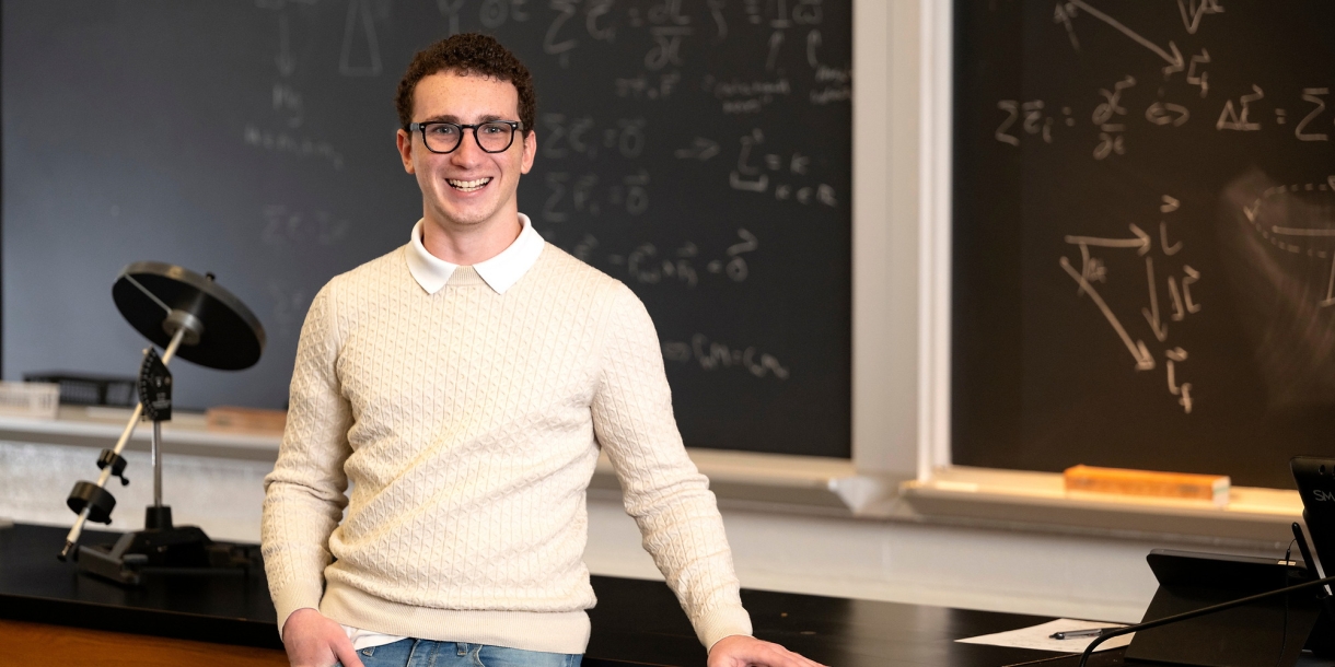 Jorge Gherson ’27 stands in a classroom with a chalkboard in the background. 