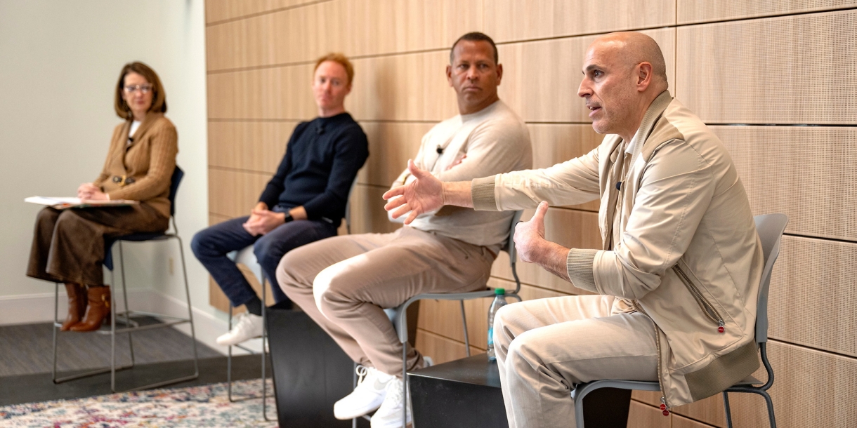 Marc Lore '93 sits on a chair on a stage and gestures with his hand as Alex Rodriguez, Jordy Leiser '06 and Dean Michelle Roehm, also in chairs on the stage, look at Marc.