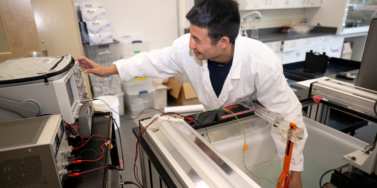 Student Tobey Kim with in a lab wearing a white lab coat and performing a test