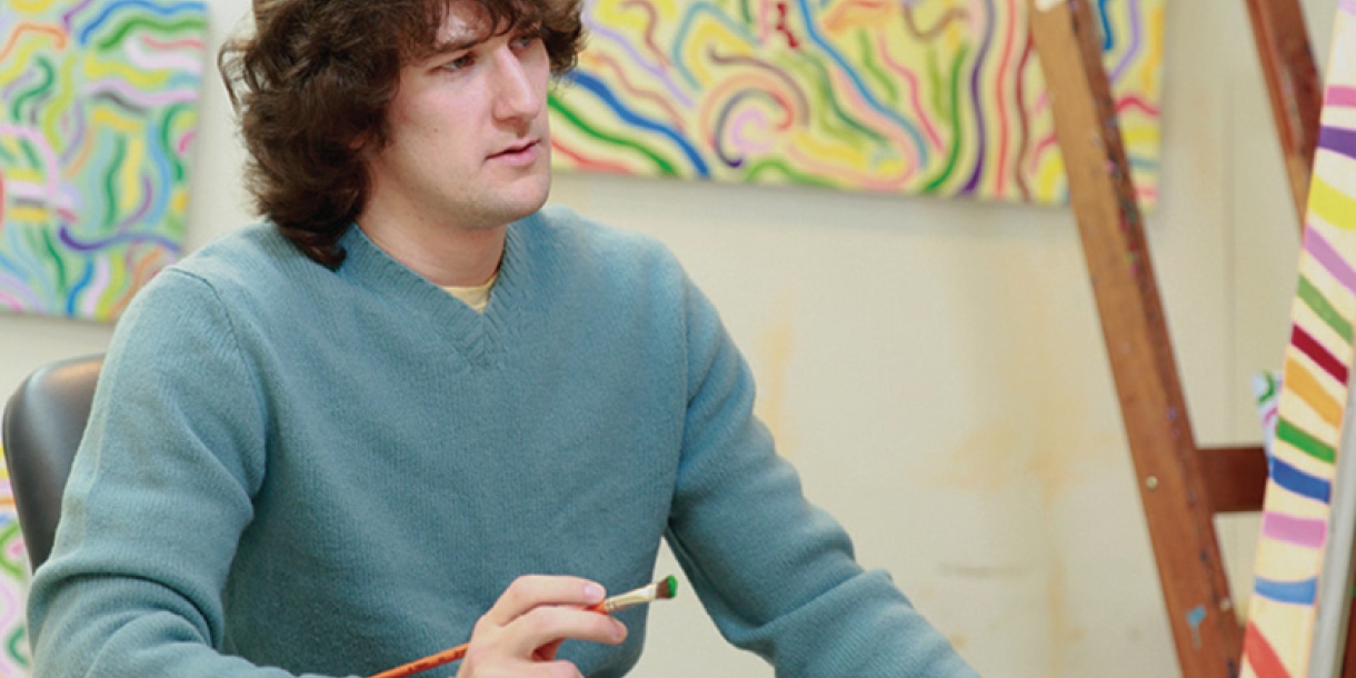 A student shown painting bright colors on a canvas