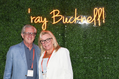 Alumni pose in front of a neon &quot;&#039;ray Bucknell&quot; sign.