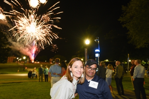 Alumni pose under fireworks.