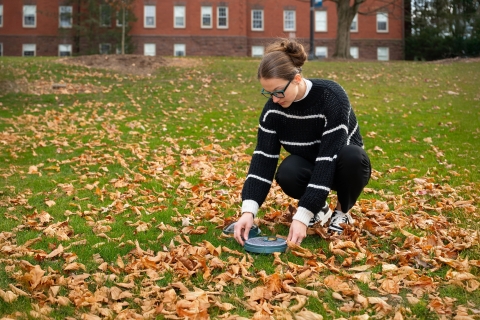 Brennah Kennedy '26 uses a Solar Pathfinder on a lawn surrounded by fallen leaves.