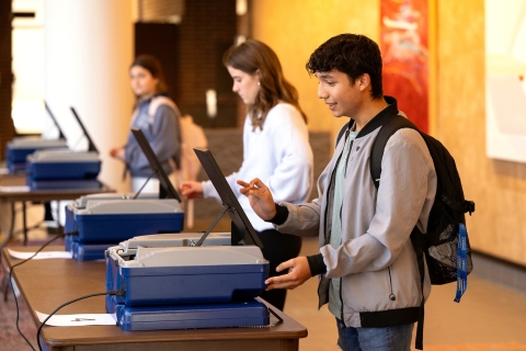 Three students stand at voting machines in the Weis Center polling location. 