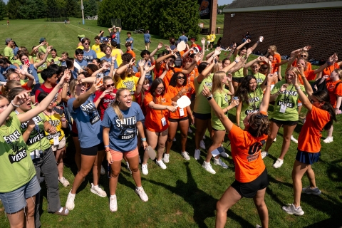 Bucknell students dance and sing while wearing a variety of blue, green, orange and yellow shirts. 