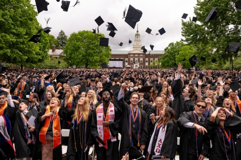 Celebratory members of the Class of 2024 toss their graduation caps in the air and cheer and smile.