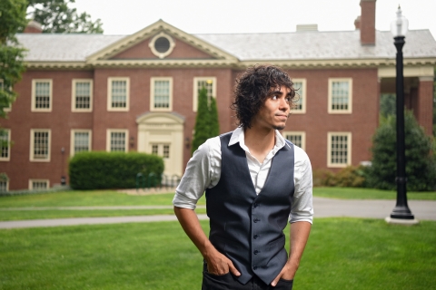​ Paul Barba wears a gray vest with white shirt and stands outside on campus looking off to his left.