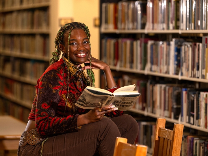 Athaliah Elvis smiles with an open book in her hand and book stacks in the background.