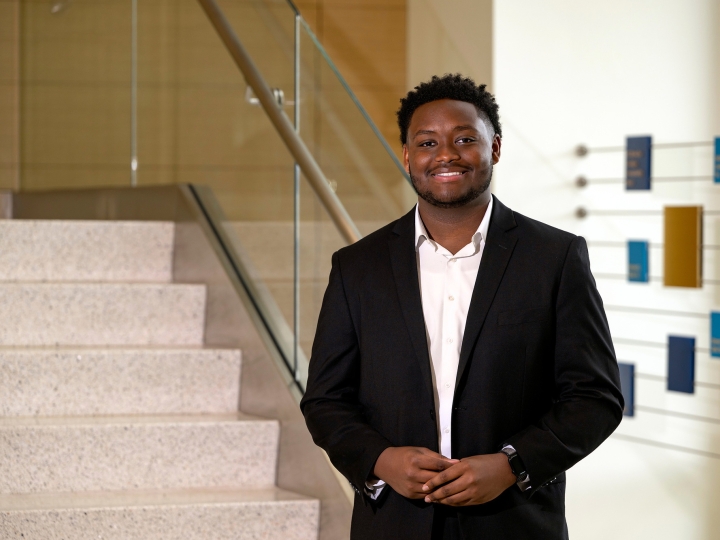 Jerimaha McClain wears a dark suit and white dress shirt and stands at the base of a stairway in Holmes Hall.