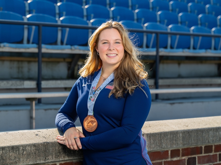 Evelyn Bliss stands on the lower level of a stadium wearing a blue Bucknell shirt and a bronze medal around her neck.