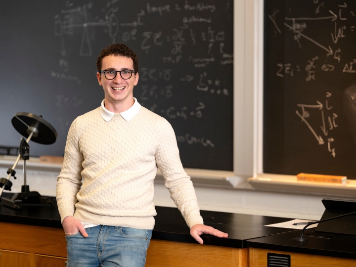 Jorge Gherson ’27 stands in a classroom with a chalkboard in the background. 