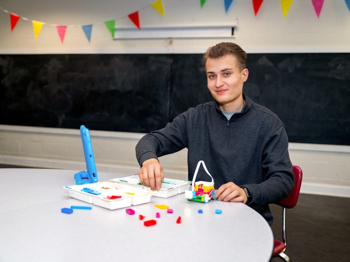 Aiden Cherniske '27 sits at a table and smiles with colorful components of robotics materials in front of him. 