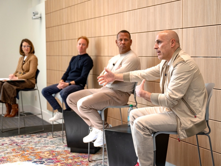 Marc Lore '93 sits on a chair on a stage and gestures with his hand as Alex Rodriguez, Jordy Leiser '06 and Dean Michelle Roehm, also in chairs on the stage, look at Marc.