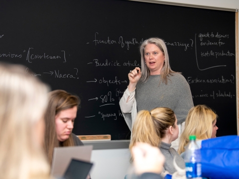 Professor Stephanie Larson stands in front of a chalk board while teaching a Women in Antiquities class.