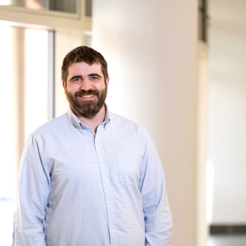 Portrait of Professor Greg O'Neill standing in a well lit hallway